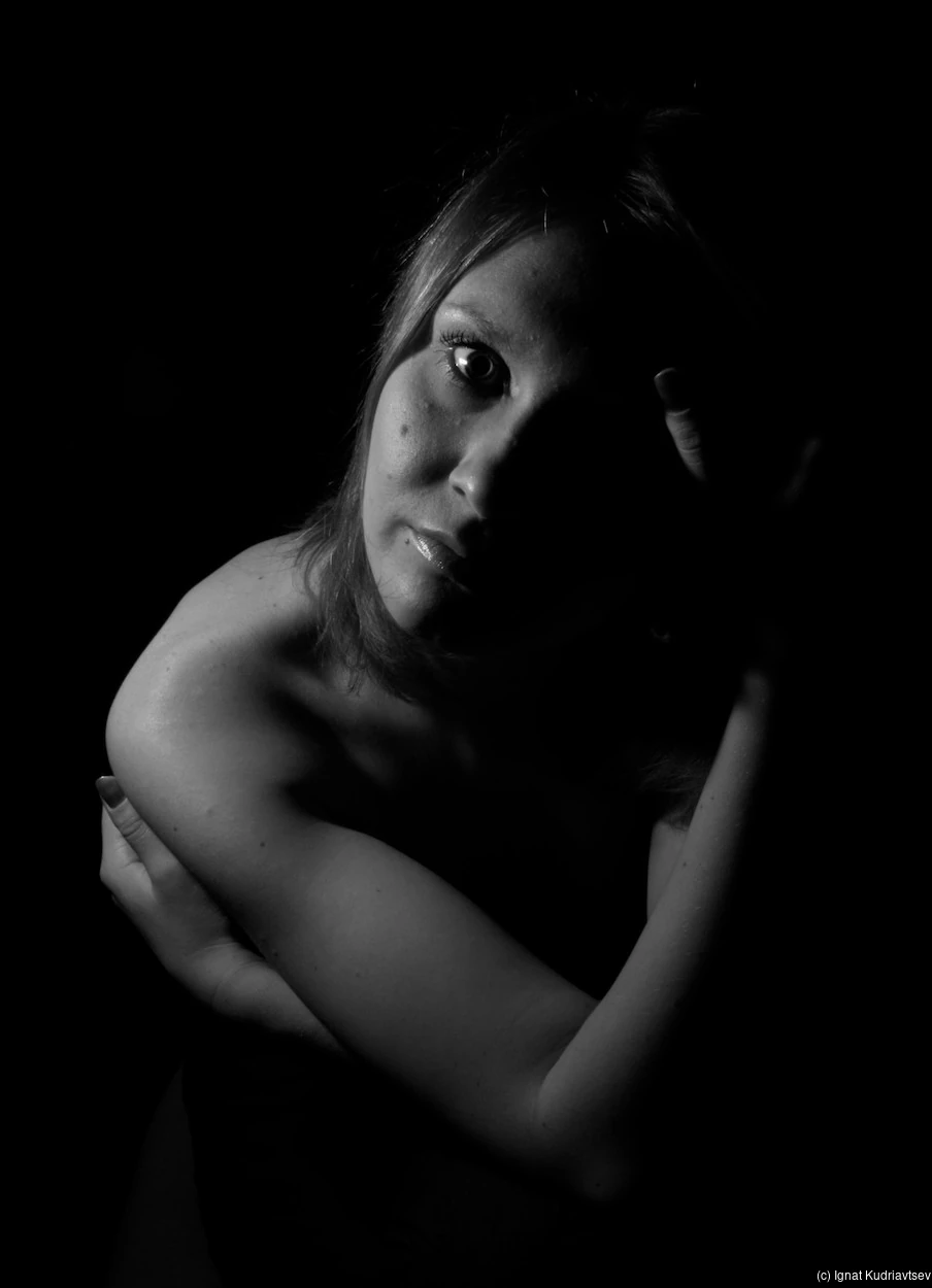 Black and white low-key portrait with one eye lit and the face partly in shadow