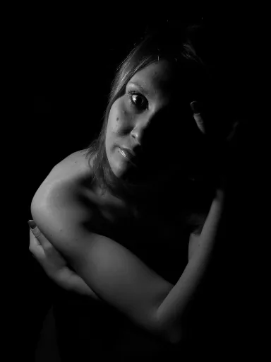 Black and white low-key portrait with one eye lit and the face partly in shadow