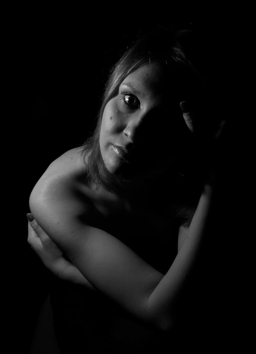 Black and white low-key portrait with one eye lit and the face partly in shadow
