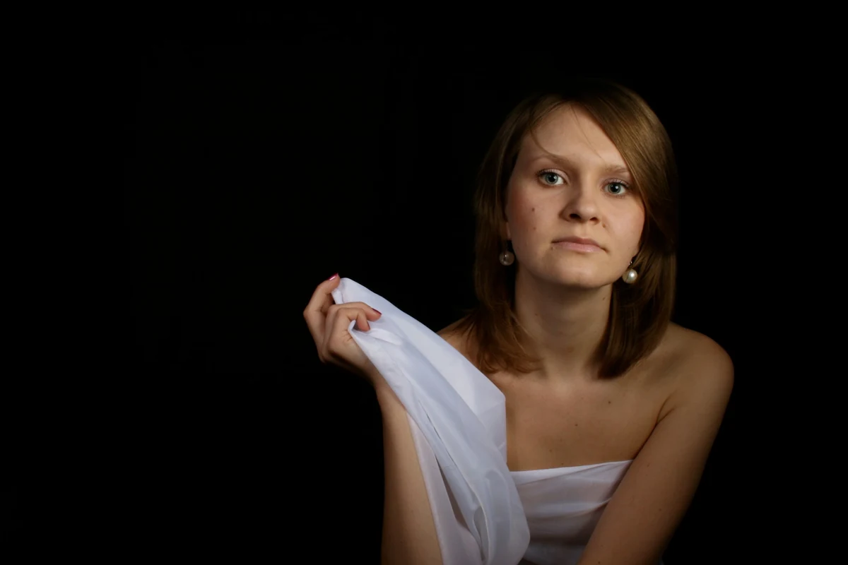Seated boudoir portrait holding white fabric against a dark studio background
