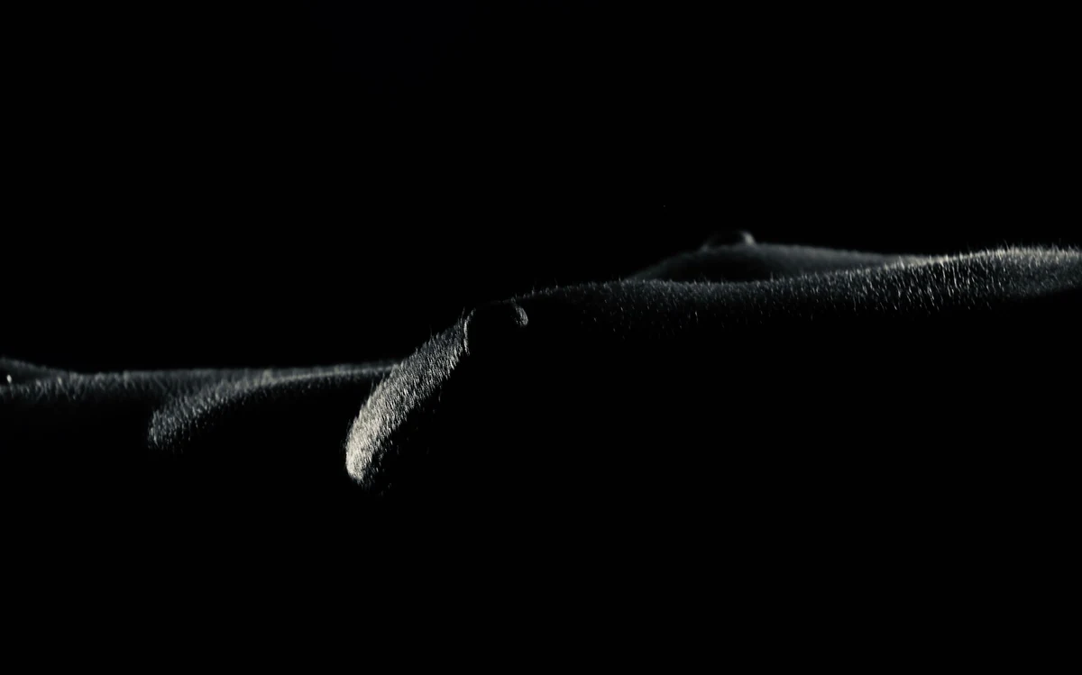 Low-key black and white detail of an outstretched arm in rim light